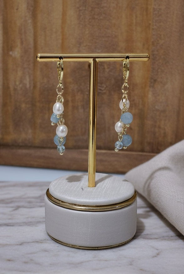 KÖRÖSSY brincos dourados com água-marinha e pérolas, design fluido e leve.